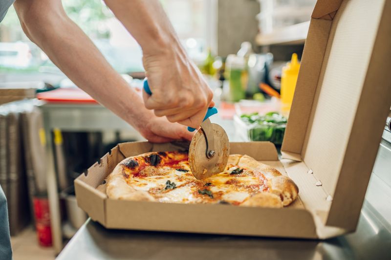 A pizza being presented by a man in the kitchen.