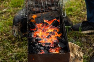 A BBQ cooking outdoors with a bonfire and person.