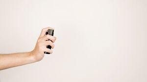 A person's hand holding a bottle of perfume.